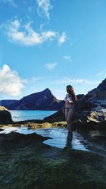 Full length of young woman standing on rock against sky