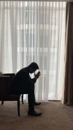 Side view of man looking through window at home