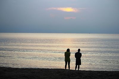 Silhouette men standing on beach against sky during sunset