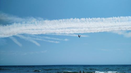 Low angle view of airplane flying over sea against blue sky
