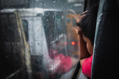 Close-up of boy by wet window in bus during rainy season