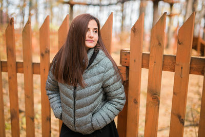 Portrait of young woman standing against fence