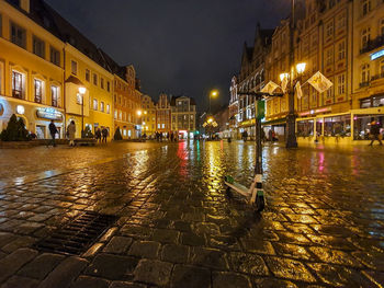 Illuminated buildings by wet street during rainy season at night