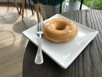 A delightful sugar glazed donut served on a white plate on a wooden table in a coffee shop