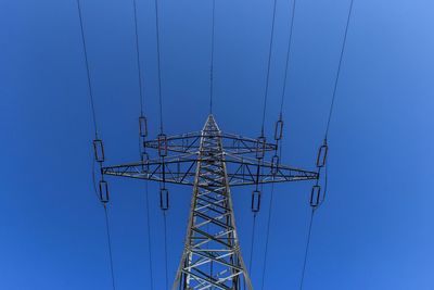 Low angle view of electricity pylon against blue sky