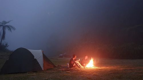 People sitting on tent against sky at night