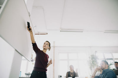 Businesswoman explaining colleagues over whiteboard during meeting in creative office