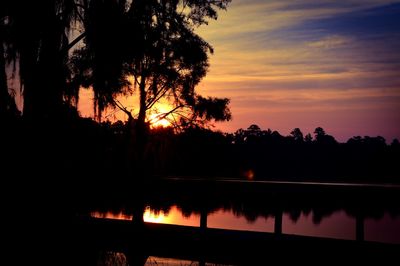 Silhouette trees by lake against sky during sunset