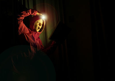 Midsection of man wearing mask against black background in darkroom