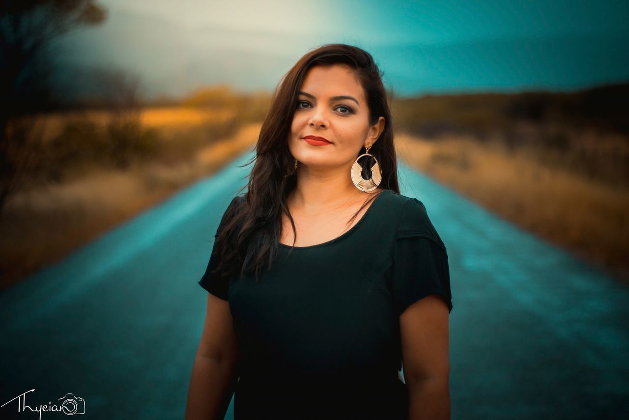 PORTRAIT OF BEAUTIFUL YOUNG WOMAN STANDING ON ROAD