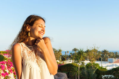 Smiling young woman with eyes closed standing against sky