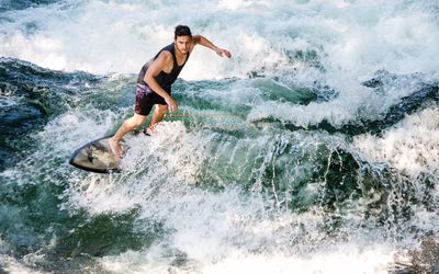 Full length of shirtless man splashing water in sea