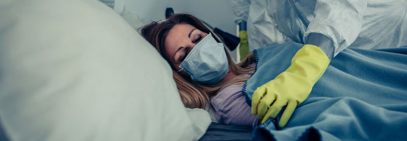 Midsection of doctor covering patient with blanket on bed