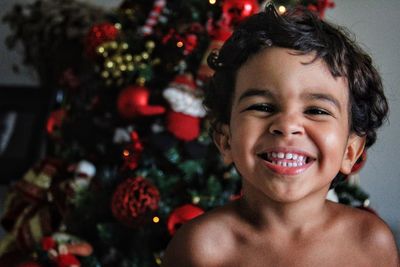 Close-up portrait of smiling boy by christmas tree