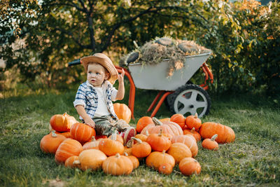 A little cowboy boy is sitting on a pumpkin in the autumn garden and trying on a hat. halloween