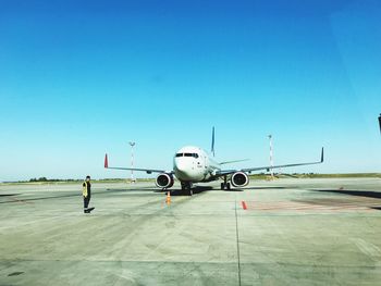 Airplane at airport runway against clear blue sky on sunny day