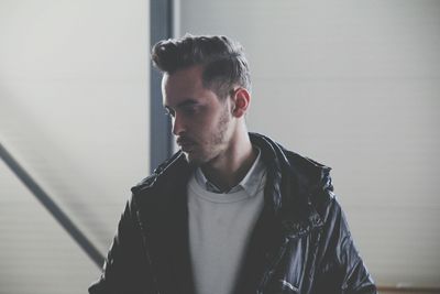 Close-up of handsome man wearing leather jacket against wall