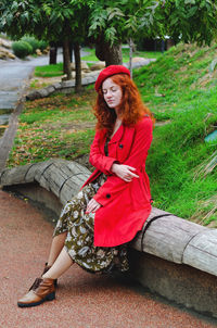 Young happy woman with red hair, freckles, beret, coat walking in autumn park, drinking coffee