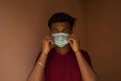 Portrait of young man with mask against wall