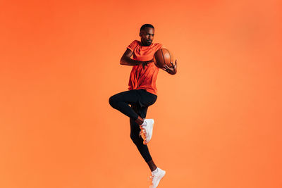 Full length of young man with arms raised against orange background