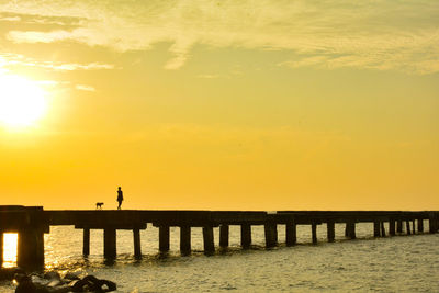 Silhouette man standing on pier over sea against sky during sunset