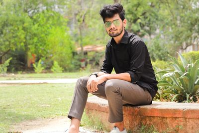 Young man looking away while sitting on plants against trees