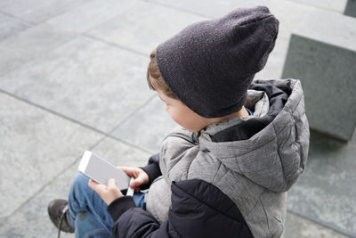 High angle view of boy using phone while sitting on seat