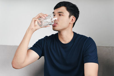 Young man drinking glass against wall