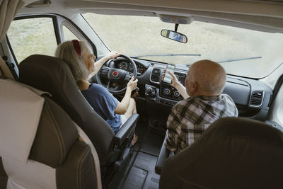 Senior man sharing smart phone with woman driving camper van during road trip