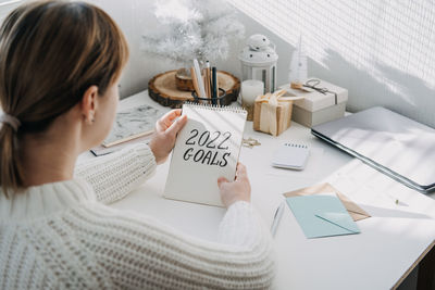 2022 goals, new year resolution. woman in white sweater writing text 2022 goals in open notepad on