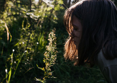 Portrait of a teenager girl looking at flower in the forest at sunset