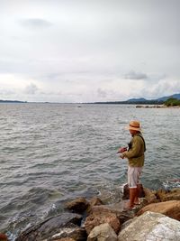 Side view of man standing on rock by sea against sky