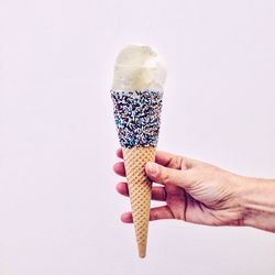Cropped hand holding ice cream cone against white background