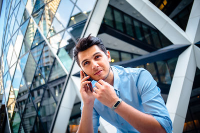 Thoughtful businessman talking on phone against modern building in city