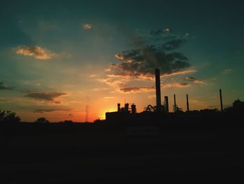 Silhouette of factory against sky at sunset