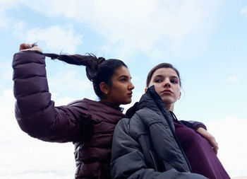 Low angle view of young friends sitting against sky