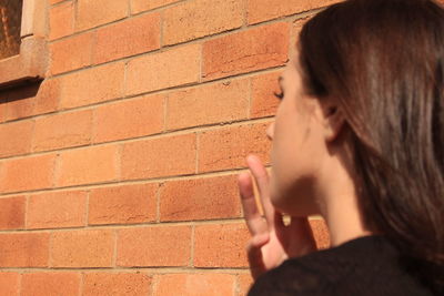 Side view of teenage girl against brick wall