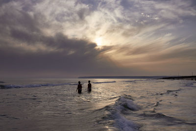 Silhouette people on beach against sky during sunset