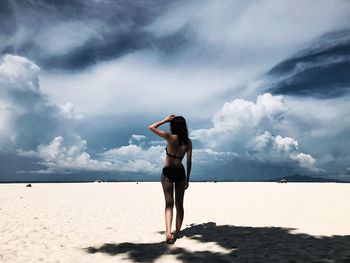 Rear view of woman walking at beach against cloudy sky