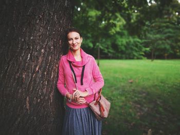 Portrait of smiling young woman standing on tree trunk