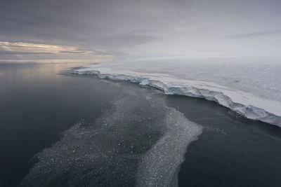 Scenic view of glacier in sea against cloudy sky during sunset