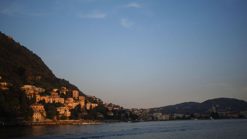 Residential buildings on tree mountain by sea against sky