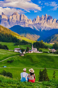 Rear view of people walking on field by mountains against sky