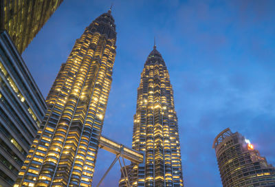 Low angle view of illuminated petronas towers against blue sky at dusk