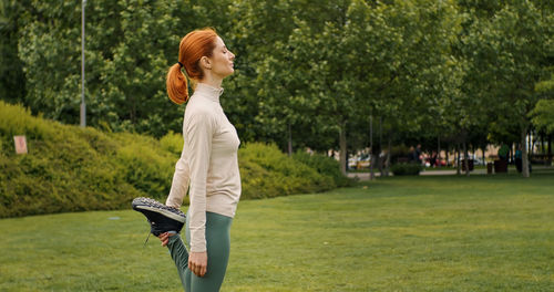 Woman do legs stretch after outdoor exercise, holding one leg up and doing legs cool-down stretching