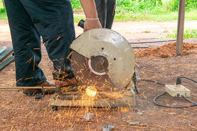 Low section of man cutting metal with circular saw at construction site