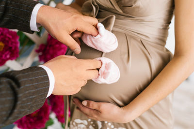 Male hands of a woman put on shoes for youth and hold them near the pregnant belly person