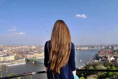 Rear view of woman with long blond hair standing at observation point in city