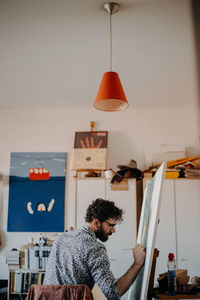 Rear view of man painting on canvas at home