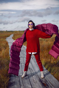 Woman  in red warm clothes and a big scarf on an ecological trail in the autumn not a swamp
